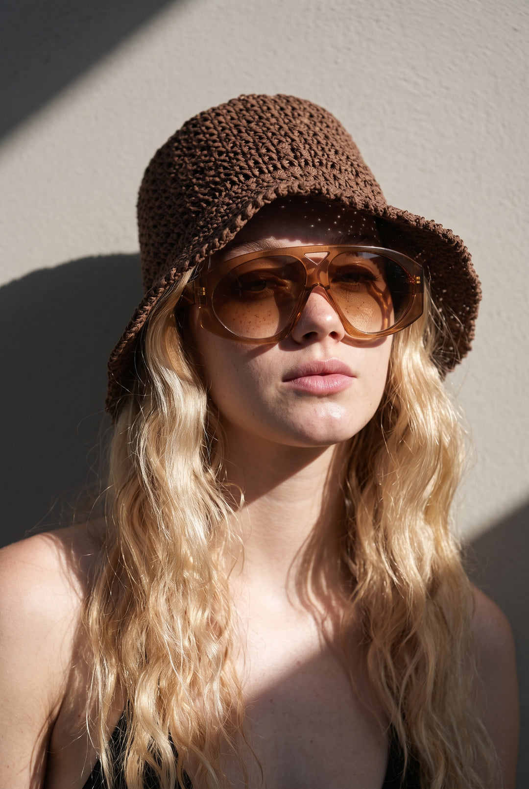 Model wearing oversized brown sunglasses and a brown woven paper straw bucket hat for beach vacations, summer travel, and everyday sun protection.